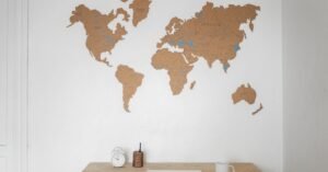 Alarm clock near pen container with cup and laptop on table placed near silhouettes of world map on wall