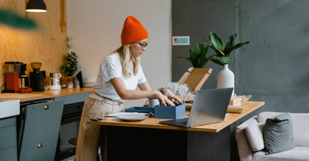 A young woman unpacks online shopping orders in a stylish modern kitchen, using her laptop for work.
